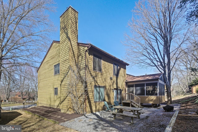 back of house with a patio, a sunroom, and a chimney