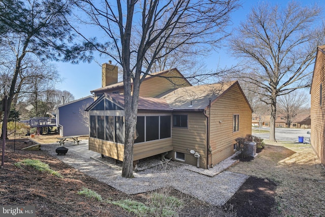 rear view of property featuring roof with shingles, a chimney, and a sunroom