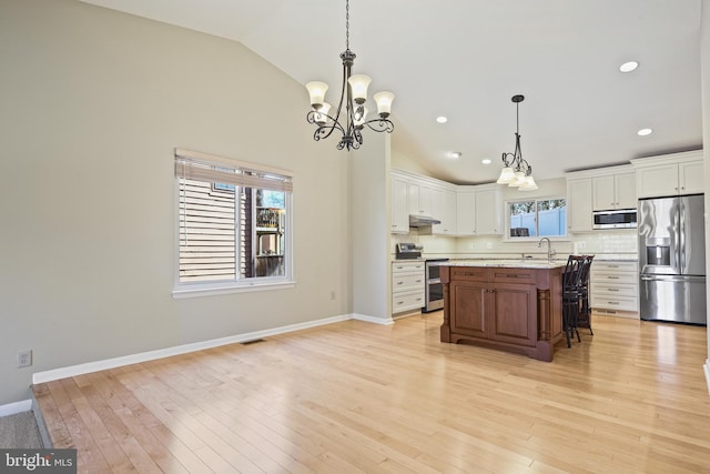 kitchen featuring under cabinet range hood, stainless steel appliances, lofted ceiling, and decorative backsplash