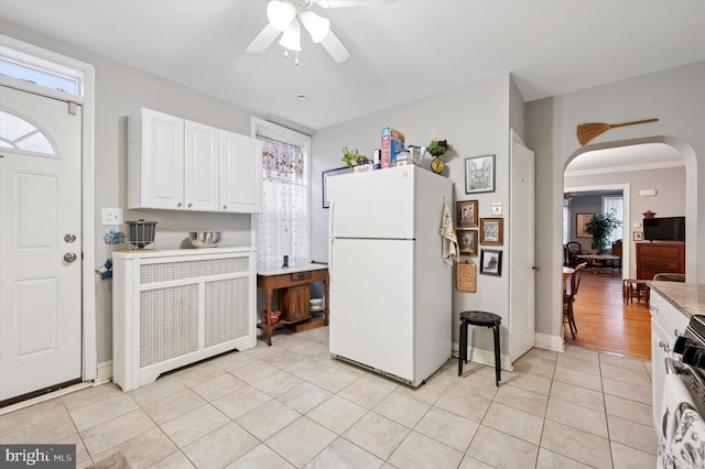 kitchen featuring light tile patterned floors, arched walkways, range, freestanding refrigerator, and white cabinetry