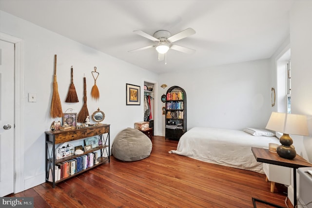 bedroom with wood finished floors, a walk in closet, and a ceiling fan