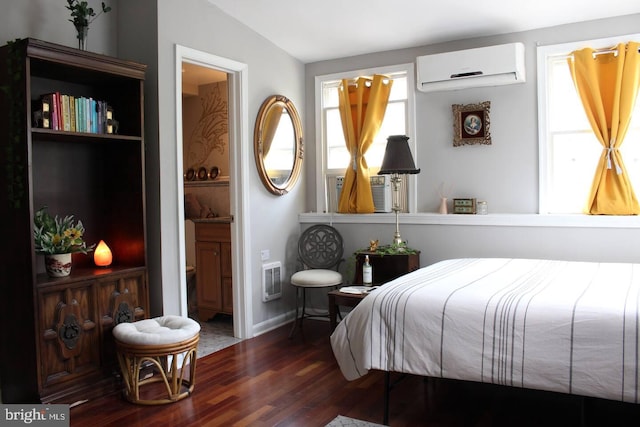 bedroom with ensuite bathroom, an AC wall unit, and wood finished floors