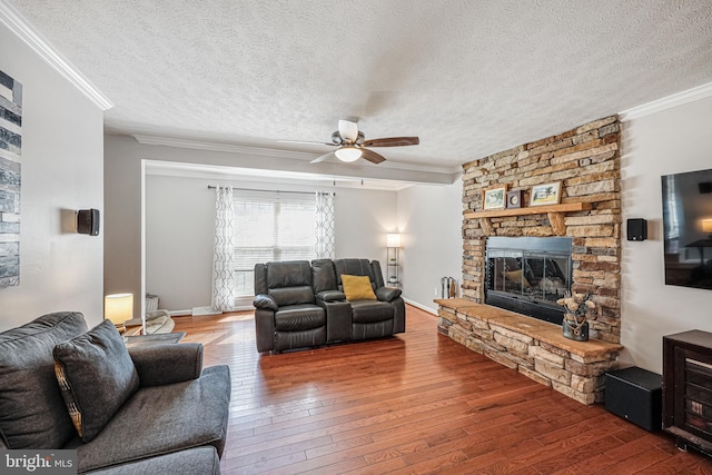 living area featuring a textured ceiling, a fireplace, a ceiling fan, hardwood / wood-style floors, and crown molding