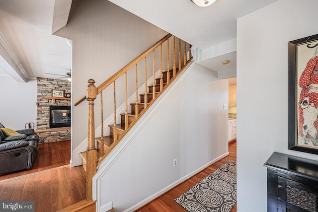 staircase featuring baseboards, a ceiling fan, wood finished floors, and a stone fireplace