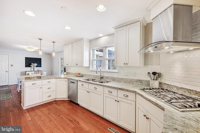 kitchen with stainless steel appliances, a peninsula, wood finished floors, a sink, and wall chimney range hood