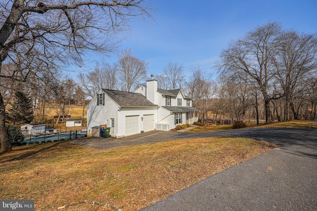 view of home's exterior featuring a chimney, fence, driveway, and a lawn