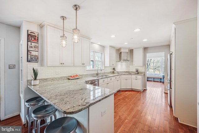 kitchen with stainless steel appliances, white cabinetry, a sink, a peninsula, and wall chimney exhaust hood