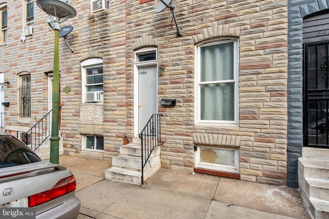 doorway to property featuring stone siding and cooling unit