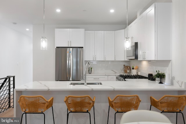 kitchen featuring a peninsula, a sink, white cabinetry, appliances with stainless steel finishes, and decorative backsplash