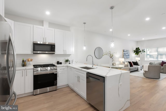 kitchen featuring stainless steel appliances, light wood finished floors, a peninsula, and a sink