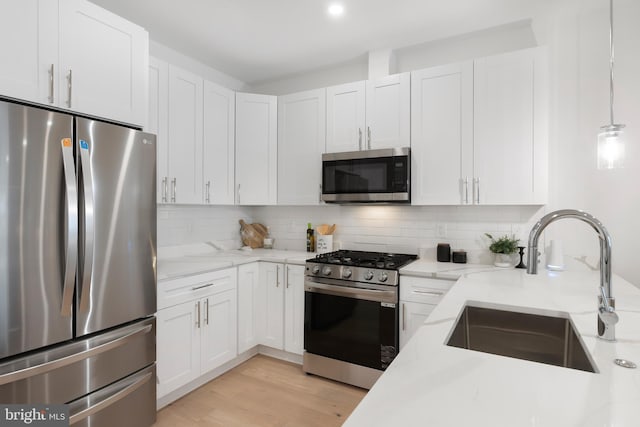 kitchen with light stone counters, stainless steel appliances, a sink, white cabinets, and decorative backsplash