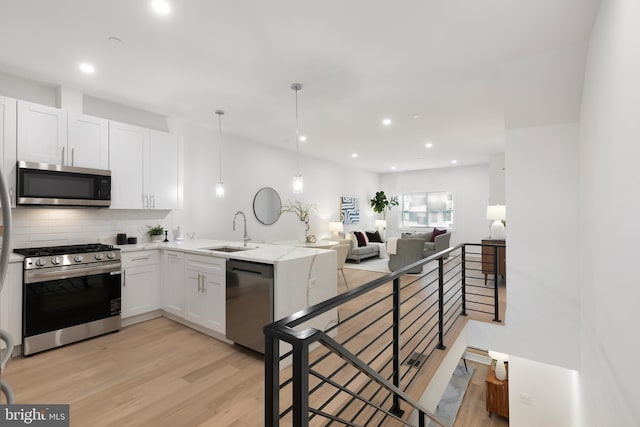 kitchen featuring light wood finished floors, appliances with stainless steel finishes, white cabinets, a sink, and a peninsula