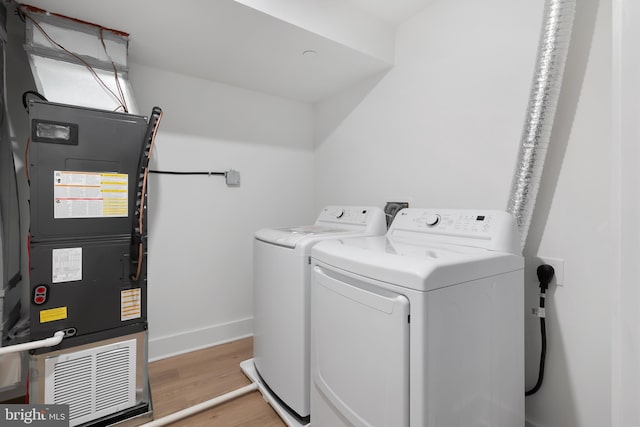 laundry room featuring laundry area, baseboards, washing machine and clothes dryer, heating unit, and light wood-type flooring