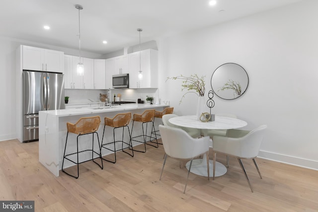 kitchen featuring a peninsula, light wood-style floors, appliances with stainless steel finishes, decorative backsplash, and a kitchen bar