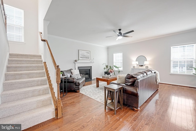 living area featuring light wood finished floors, a glass covered fireplace, stairs, and ornamental molding