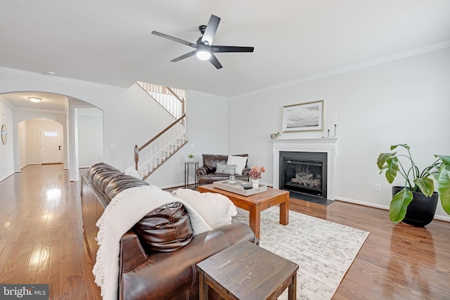 living room with hardwood / wood-style flooring, a fireplace with flush hearth, arched walkways, and ornamental molding