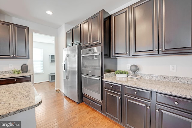 kitchen featuring light stone counters, dark brown cabinets, appliances with stainless steel finishes, and light wood-style floors