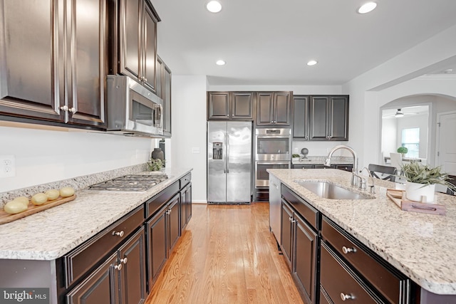 kitchen featuring light wood-style flooring, a sink, recessed lighting, arched walkways, and appliances with stainless steel finishes