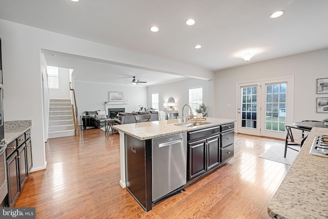 kitchen with light wood finished floors, dishwasher, an island with sink, a fireplace, and a sink