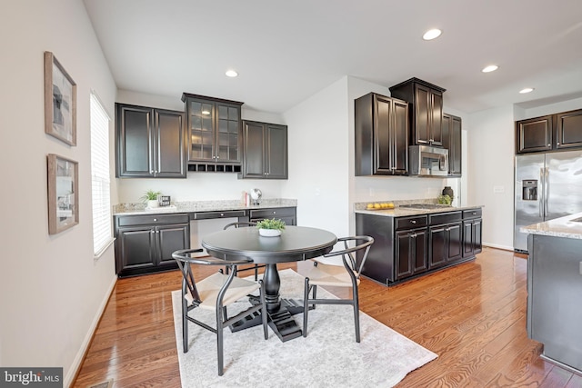 kitchen with glass insert cabinets, baseboards, light wood-type flooring, recessed lighting, and appliances with stainless steel finishes