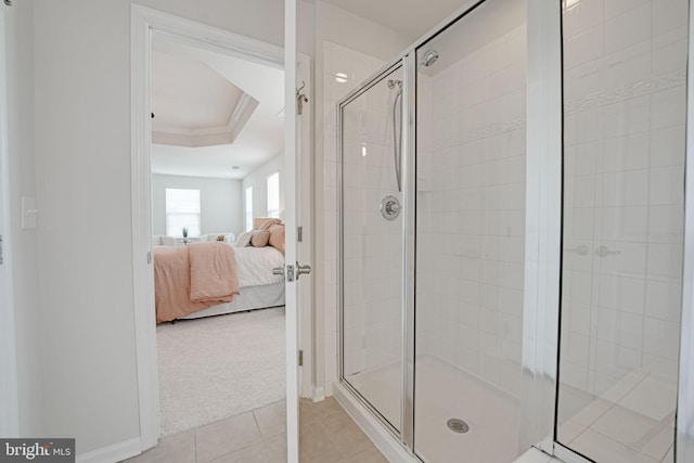 ensuite bathroom featuring tile patterned flooring, a tray ceiling, ornamental molding, a stall shower, and ensuite bathroom