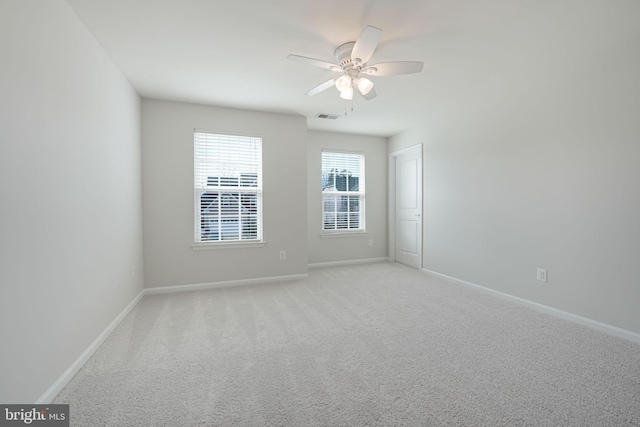 empty room with a ceiling fan, light colored carpet, visible vents, and baseboards