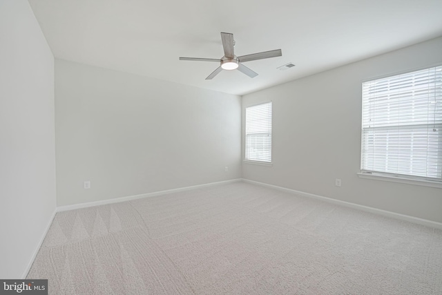 unfurnished room with ceiling fan, light colored carpet, visible vents, and baseboards