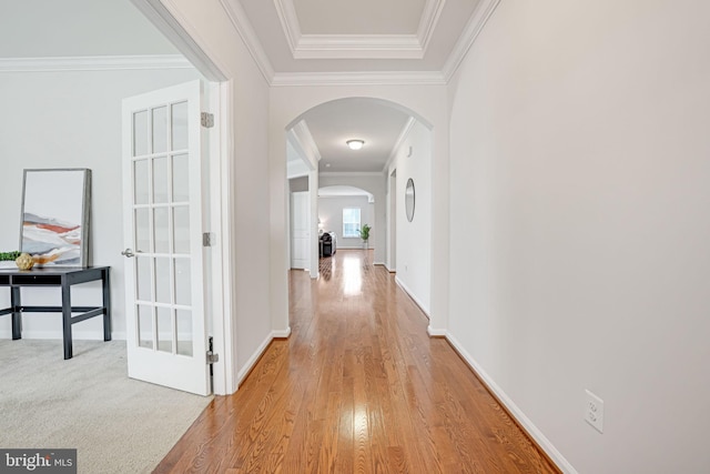 hall featuring arched walkways, light wood finished floors, crown molding, and baseboards