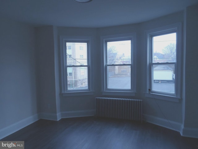 spare room with dark wood-style flooring, baseboards, and radiator heating unit