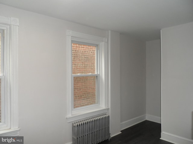 unfurnished room with radiator heating unit, baseboards, and dark wood-type flooring