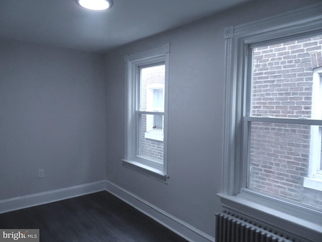 spare room featuring dark wood-type flooring, radiator, and baseboards