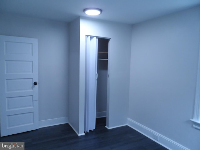 unfurnished bedroom with dark wood-style floors, a closet, and baseboards