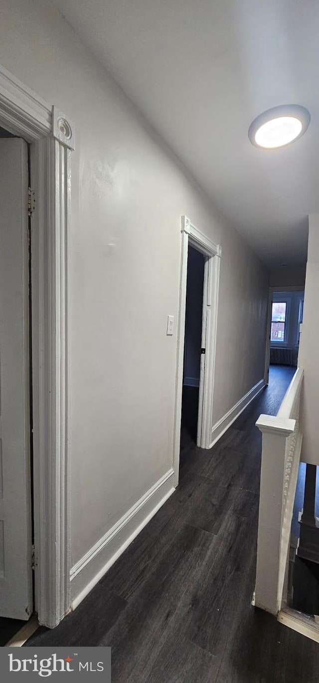 corridor featuring baseboards, wood finished floors, and an upstairs landing