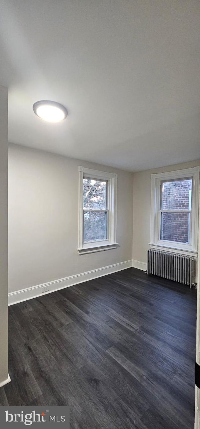 spare room featuring dark wood-type flooring, baseboards, and radiator heating unit