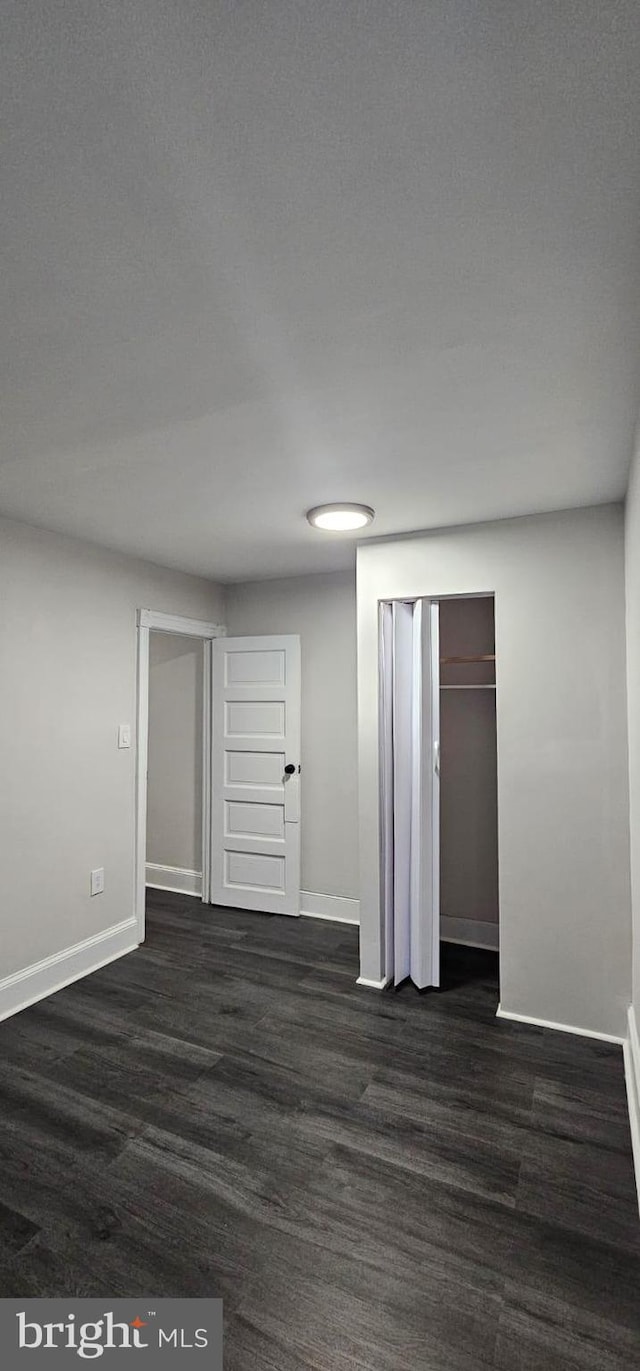 unfurnished bedroom with baseboards and dark wood-style flooring