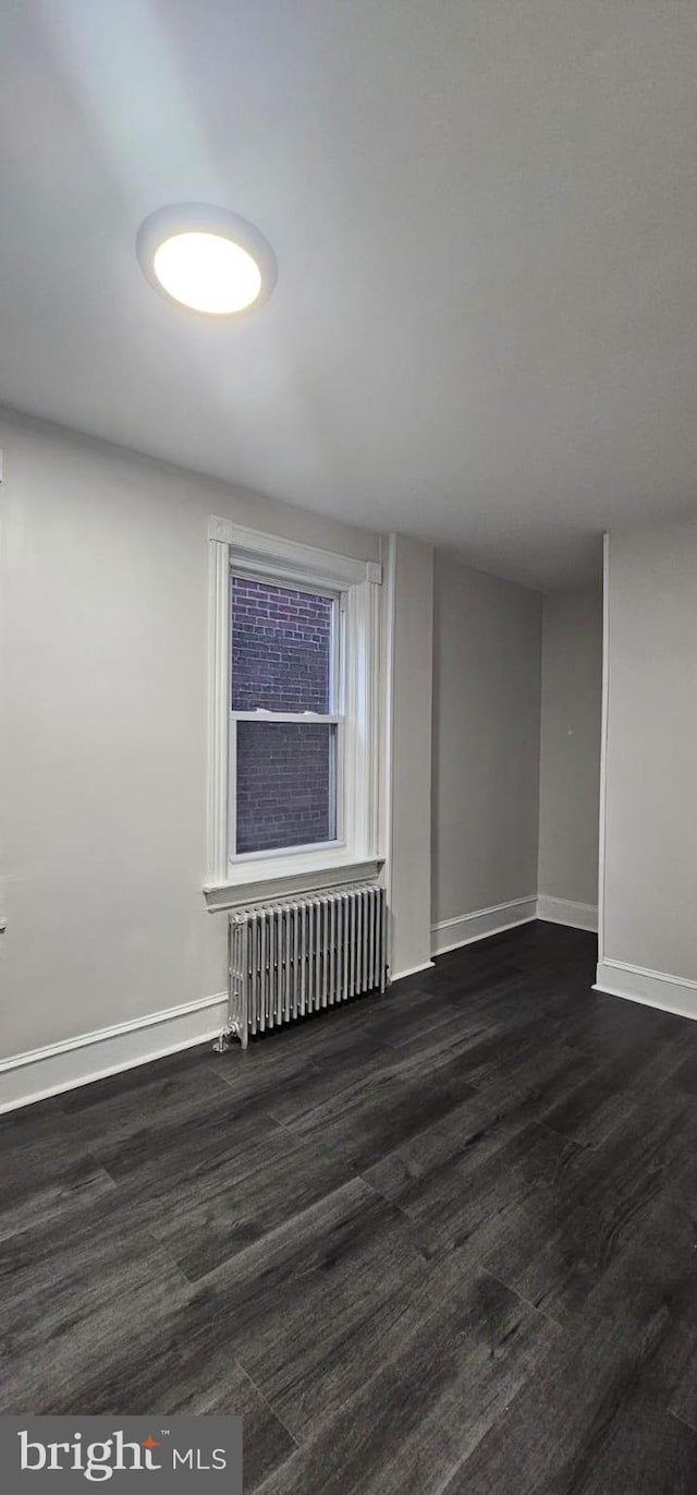 empty room with radiator heating unit, baseboards, and dark wood-type flooring