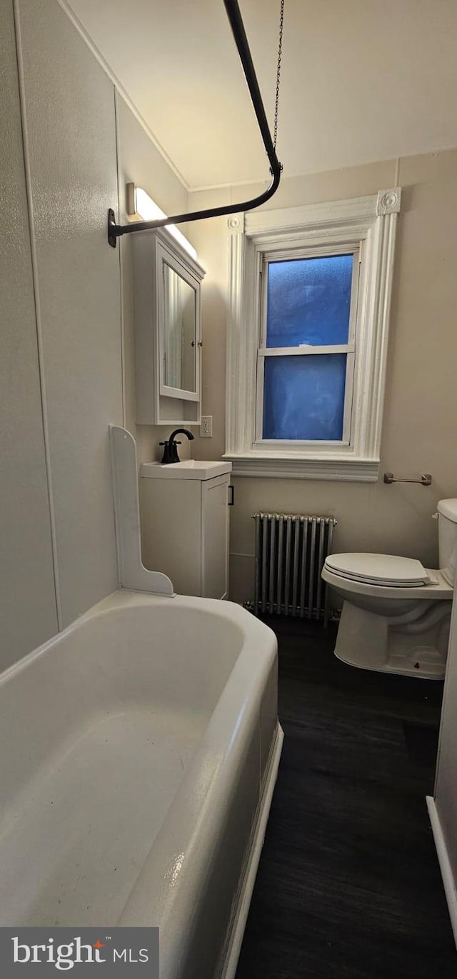 full bath with a tub to relax in, wood finished floors, toilet, and radiator