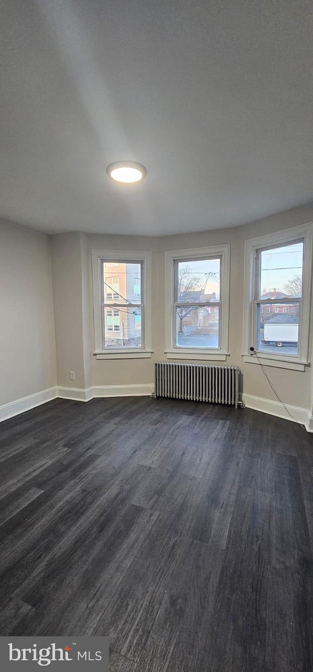 spare room with dark wood-style flooring, baseboards, and radiator heating unit