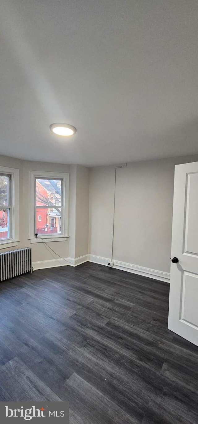 empty room with dark wood-style flooring, baseboards, and radiator heating unit