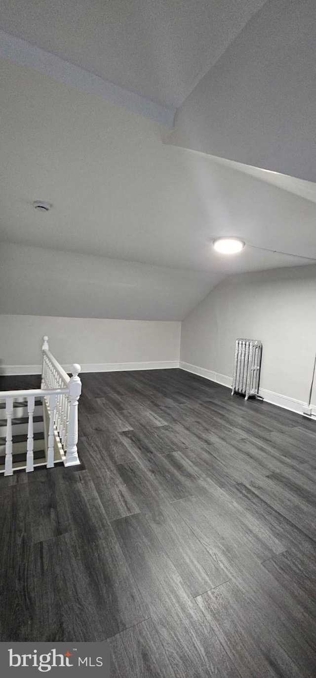 additional living space featuring vaulted ceiling, dark wood-type flooring, and baseboards