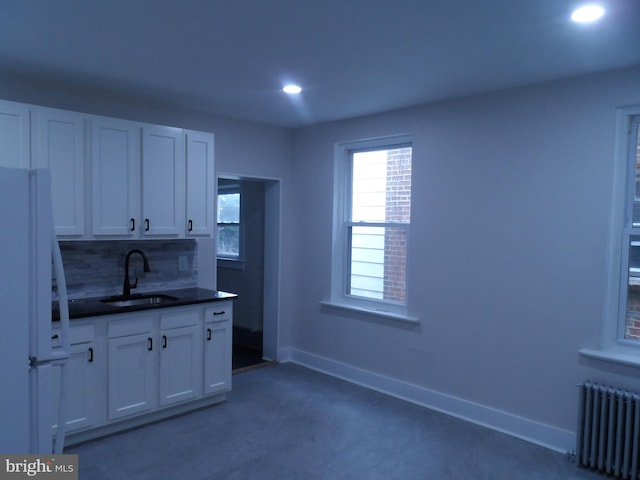 kitchen featuring baseboards, dark countertops, radiator heating unit, freestanding refrigerator, and a sink