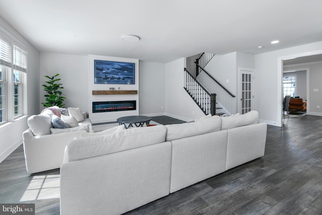 living room featuring dark wood-style floors, stairs, baseboards, and a glass covered fireplace