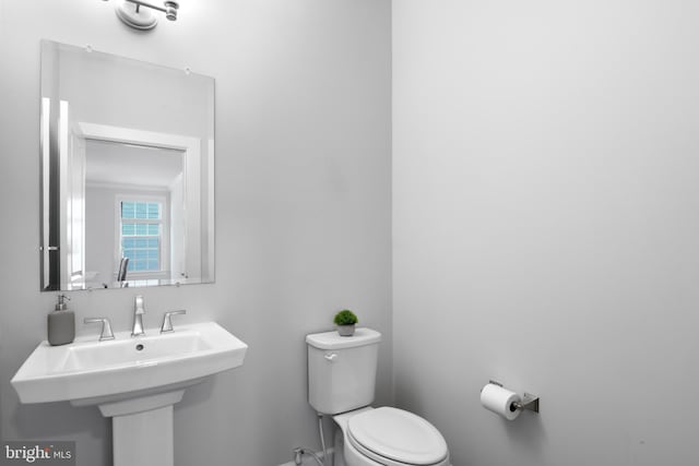 half bath with baseboards, a sink, and toilet