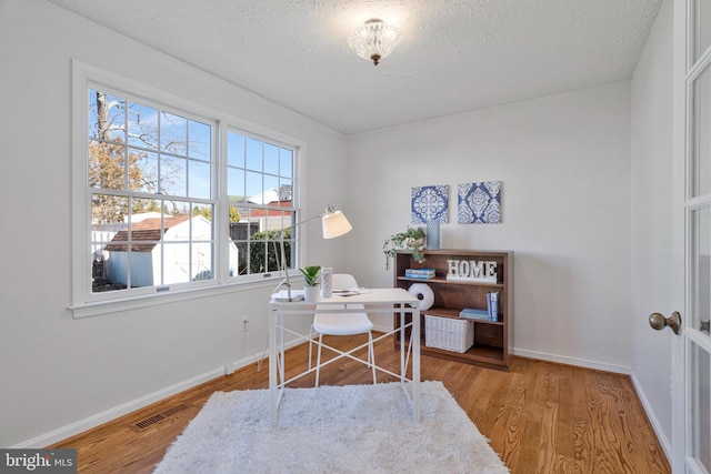 office featuring visible vents, a textured ceiling, baseboards, and wood finished floors