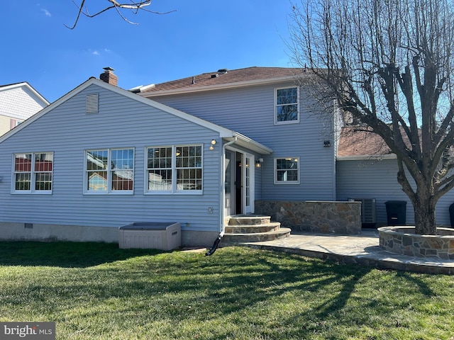 rear view of property with crawl space, a patio area, a lawn, and a chimney