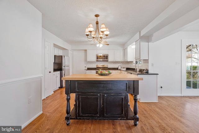 kitchen featuring stainless steel appliances, wooden counters, backsplash, white cabinets, and a chandelier