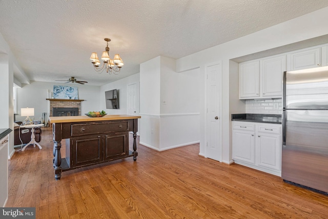 kitchen with white cabinets, light wood-style flooring, a fireplace, and stainless steel refrigerator