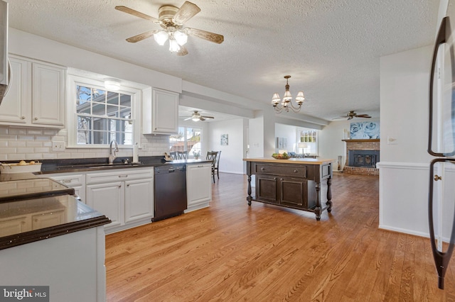 kitchen with black dishwasher, open floor plan, light wood-type flooring, white cabinetry, and a sink