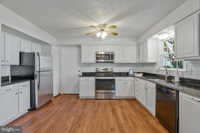 kitchen featuring stainless steel appliances, dark countertops, a sink, and white cabinets