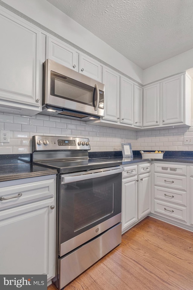 kitchen featuring tasteful backsplash, dark countertops, stainless steel appliances, light wood-type flooring, and white cabinetry